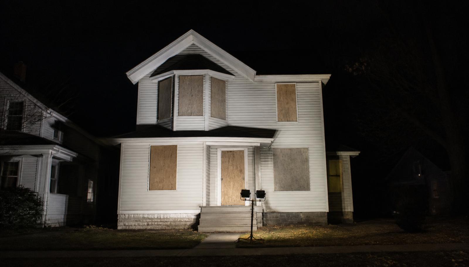 Boarded up home at night lit by portable work lights