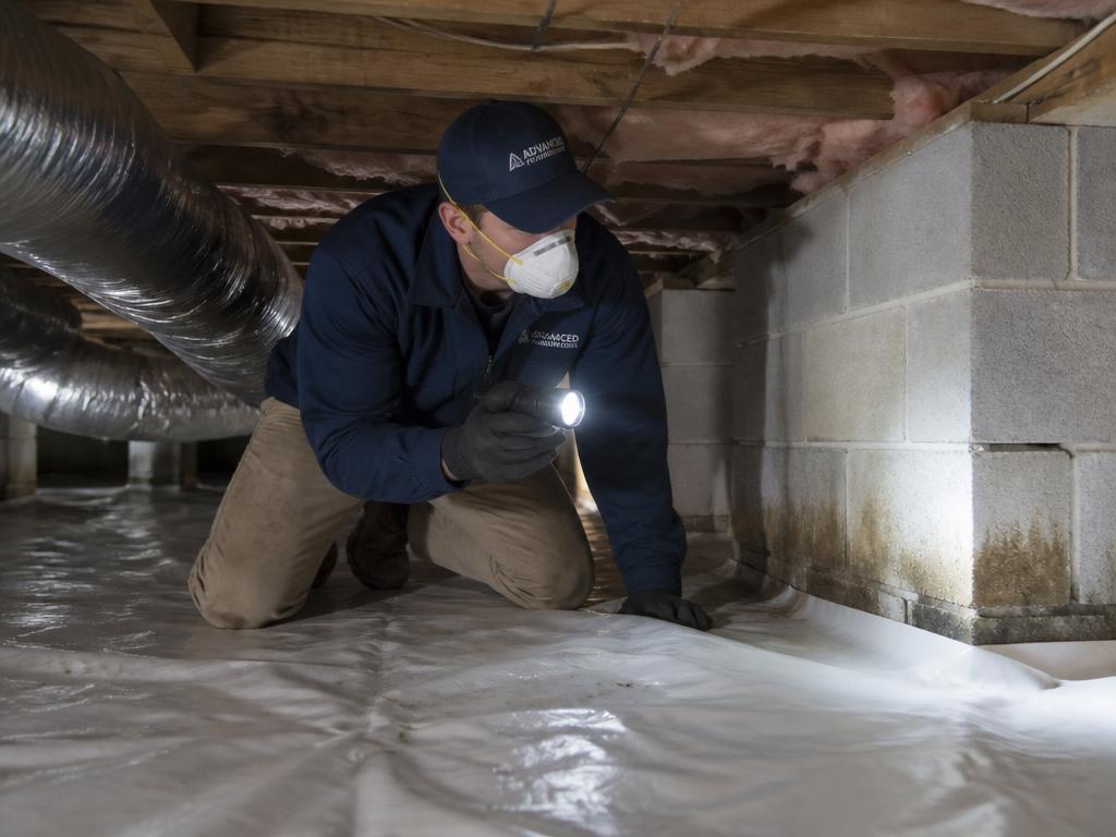 Technician inspecting a damp crawl space with a flashlight in Central Indiana